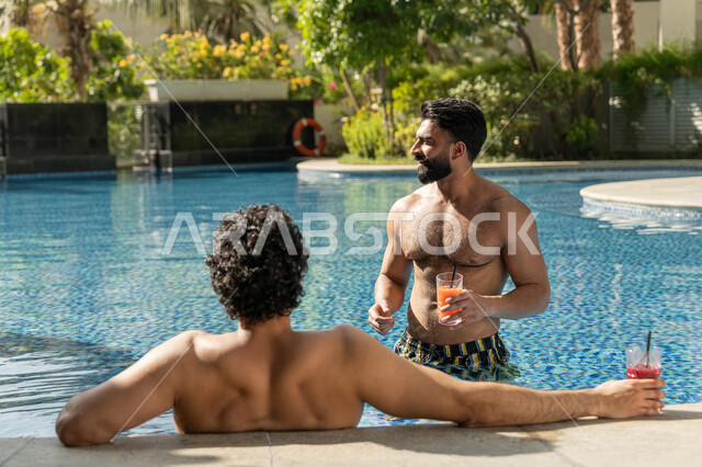 الاستمتاع بالمشروبات الباردة المنعشة, القيام بالأنشطة الترفيهية المسلية, مشاركة الأصدقاء اللحظات الممتعة, قضاء العطلة الصيفية في المنتجعات السياحية, شابان عربيان خليجيان إماراتيان يجلسان داخل حوض السباحة في إحدى الفنادق بالإمارات