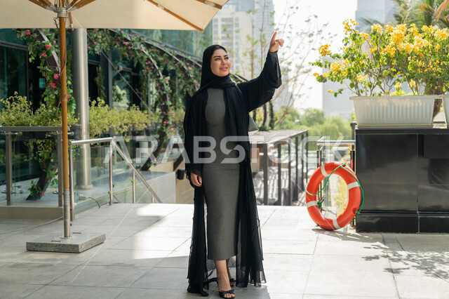 الاستمتاع بالعطلة الصيفية, قضاء الأوقات الممتعة في المنتجعات والفنادق, القيام بالأنشطة الترفيهية المسلية في الإجازة, امرأة عربية خليجية إماراتية محجبة ترتدي الزي الكاجوال تشير بإصبع السبابة إلى شيء ما بالأعلى