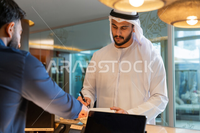 القيام بإجراءات الحجز والدخول, قضاء أوقات ممتعة في العطلة الصيفية, منتجعات وفنادق الإمارات العربية المتحدة, رجل عربي خليجي إماراتي يرتدي الكندورة والغترة البيضاء يقوم بتسجيل المعلومات والبيانات الشخصية