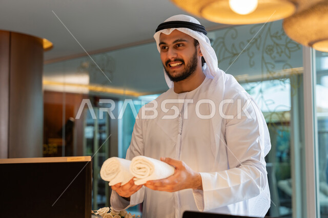 Enjoying summer vacation, hotels and resorts in UAE, spending time on vacation, smiling Emirati Gulf Arab man wearing white kandura and ghutra taking towels from reception, summer fun trips