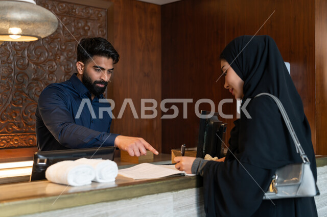 القيام بإجراءات الحجز والدخول, منتجعات وفنادق الإمارات العربية المتحدة, قضاء أوقات ممتعة في العطلة الصيفية, موظف استقبال عربي خليجي إماراتي يرتدي الزي الرسمي يقوم بالشرح عن أنواع الغرف والإقامات للمرأة