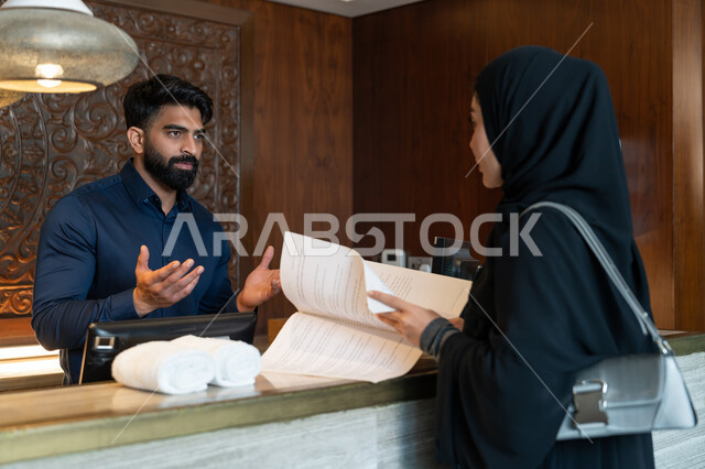 منتجعات وفنادق الإمارات العربية المتحدة, القيام بإجراءات الحجز والدخول, قضاء أوقات ممتعة في العطلة الصيفية, موظف استقبال عربي خليجي إماراتي يرتدي الزي الرسمي يقوم بالشرح عن أنواع الغرف والإقامات للمرأة