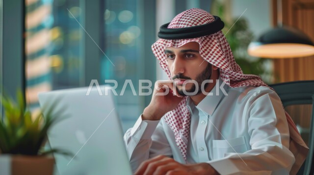 Using modern and advanced technological devices, managing and organizing business affairs, office administrative professions and jobs, a close-up image from the side of a Saudi Arabian Gulf employee wearing a traditional thobe and shemagh working on a computer inside the office