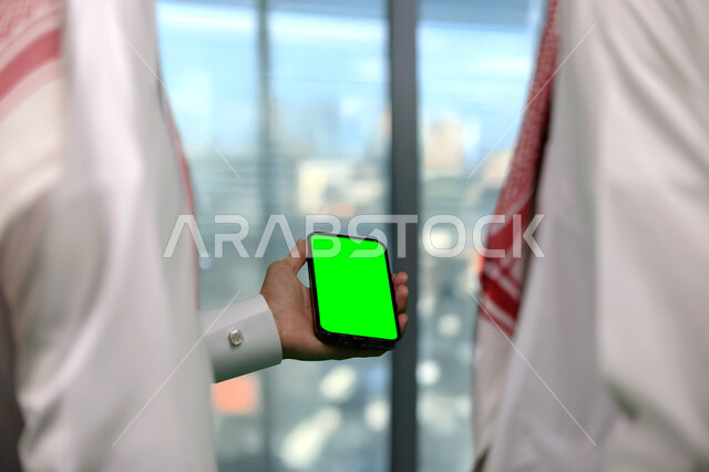 القيام بالدردشات والمحادثات مع العائلة والأصدقاء، إنجاز مهام العمل عبر الإنترنت بين زملاء العمل، تصوير مقرب لرجل عربي خليجي سعودي يحمل بيده الهاتف المحمول، أجهزة إلكترونية بشاشة خضراء فارغة, كروما