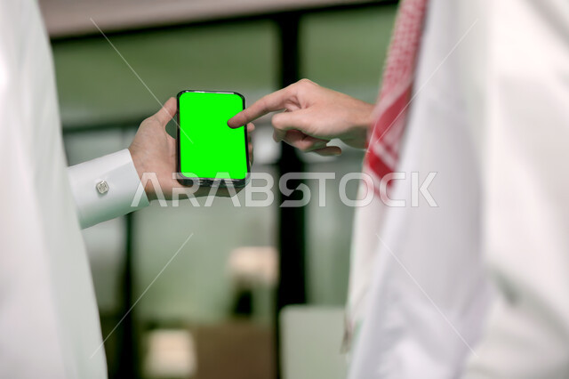 القيام بالدردشات والمحادثات مع العائلة والأصدقاء، إنجاز مهام العمل عبر الإنترنت بين زملاء العمل، تصوير مقرب لرجل عربي خليجي سعودي يحمل بيده الهاتف المحمول، أجهزة إلكترونية بشاشة خضراء فارغة, كروما