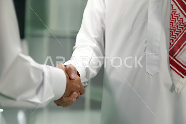 الإتفاق والشراكة على الأعمال والمشاريع التجارية, صورة مقربة لرجلان عربيان خليجيان سعوديان يرتديان الزي التقليدي يتصافحان لنجاح الصفقة داخل مقر الشركة, مهن وأعمال تجارية 