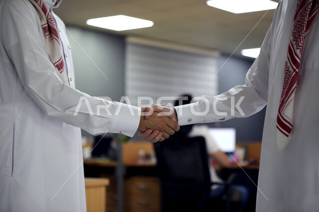 Agreement and partnership on business and commercial projects, close-up of two Saudi Arabian Gulf men wearing traditional dress shaking hands to make the deal a success inside the company headquarters, professions and commercial businesses