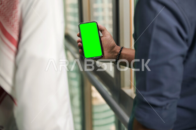 القيام بالدردشات والمحادثات مع العائلة والأصدقاء، إنجاز مهام العمل عبر الإنترنت بين زملاء العمل، صورة مقربة لرجل عربي خليجي سعودي يحمل بيده الهاتف المحمول، أجهزة إلكترونية بشاشة خضراء فارغة, كروما