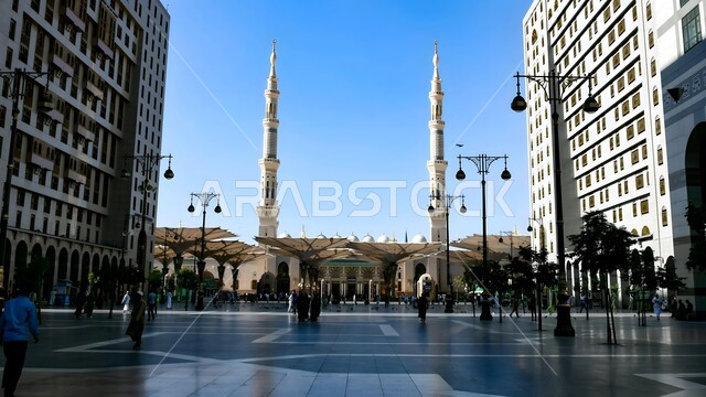 مفهوم العبادة والطاعة والتقرب الى الله، المظلات الإلكترونية في ساحة مسجد رسول الله في المدينة المنورة في وقت النهار، أماكن ومعالم دينية مقدسة في المملكة العربية السعودية، تجمع المسلمون في الساحة الخارجية للمسجد النبوي، الفن الهندسي المعماري لبناء المساجد والمآذن على الطراز الاسلامي