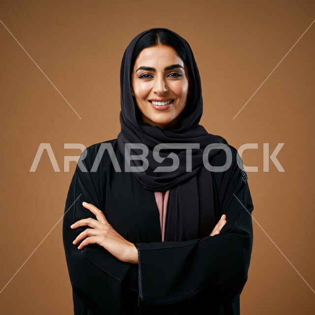ملابس وأزياء محجبات عصرية راقية، الملامح العربية الأصيلة، مفهوم الثقة بالنفس والاهتمام بالمظهر الخارجي، بورتريه مقرب لامرأة عربية خليجية سعودية مبتسمة ترتدي الحجاب والعباءة تنظر الى الكاميرا بتعابير السرور تقف بأيدي متقاطعة، خلفية بنية 