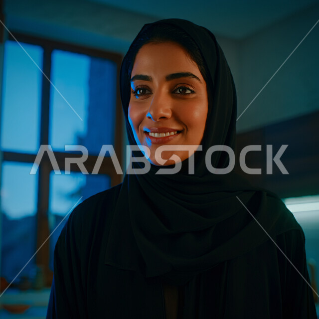 أزياء محجبات عصرية راقية، قضاء اوقات ممتعة في المنزل، الهدوء والاسترخاء والراحة، مفهوم الأناقة والاهتمام بالمظهر الخارجي، صورة مقربة لامرأة عربية خليجية سعودية مبتسمة ترتدي العباءة والحجاب تنظر الى شيء ما بإيماءات السرور و الثقة بالنفس