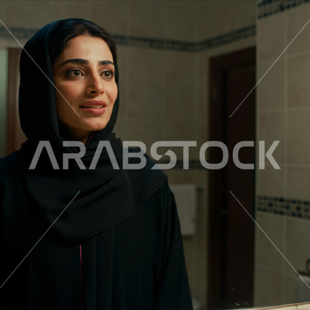 قضاء اوقات ممتعة في المنزل، الهدوء والاسترخاء والراحة، أزياء محجبات عصرية راقية، مفهوم الأناقة والاهتمام بالمظهر الخارجي، صورة مقربة لامرأة عربية خليجية سعودية مبتسمة ترتدي العباءة والحجاب تنظر الى شيء ما بإيماءات السرور و الثقة بالنفس