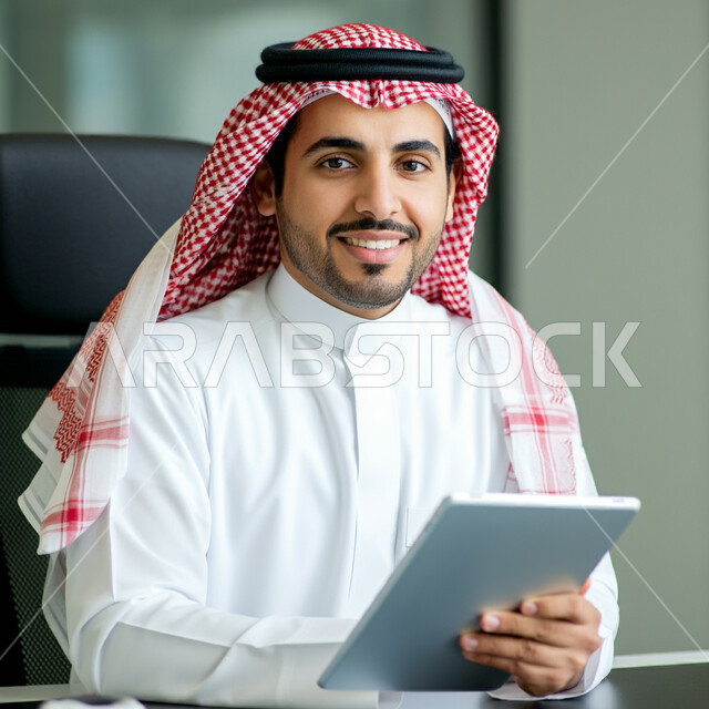 استخدام الأجهزة التقنية الحديثة، تصفح مواقع التواصل الاجتماعي والتواصل مع الأهل والأصدقاء، صورة مقربة لرجل عربي خليجي سعودي يرتدي الثوب التقليدي والشماغ يمسك الجهاز اللوحي ينظر إلى الكاميرا بإيماءات الثقة، مفهوم إنجاز المشاريع ومهام العمل عن بعد