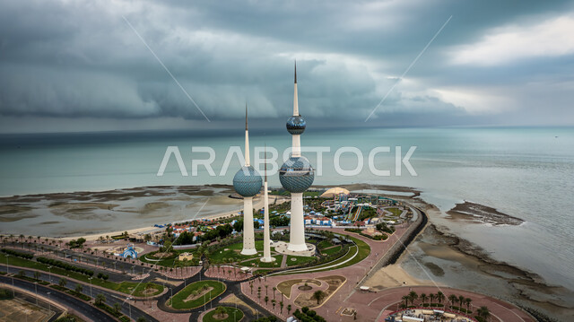 الفن الهندسيي المعماري لابراج مدينة الكويت, ناطحات السحاب والمنشآت على ساحل الخليج العربي في منطقة رأس عجوزة, التطور والتقدم العمراني على الطراز الحديث, معالم سياحية مشهورة, منظر السماء المليئة بالغيوم الداكنة, الاشجار والنباتات الخضراء في الطرقات الكويتية
