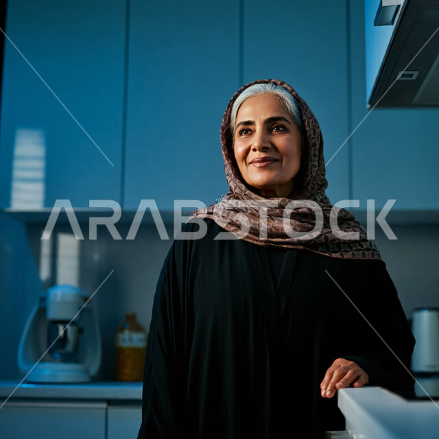 قضاء اوقات ممتعة في المنزل، الهدوء والاسترخاء والراحة، أزياء محجبات عصرية راقية، مفهوم الأناقة والاهتمام بالمظهر الخارجي، صورة مقربة لامرأة عربية خليجية سعودية مبتسمة ترتدي العباءة والحجاب تنظر الى شيء ما بإيماءات السرور و الثقة بالنفس