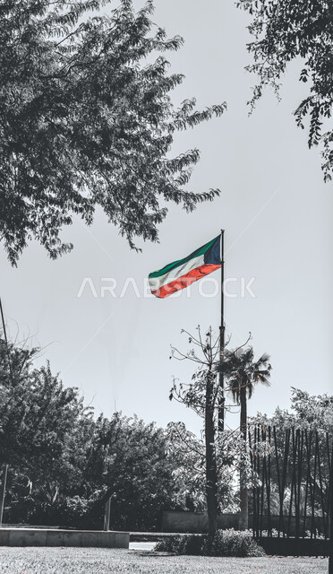 العلم الكويتي بألوانه الأربعة الزاهية يرفرف على سارية عاليا في الهواء، الأماكن والمعالم الترفيهية العائلية، حديقة الشهيد بمدينة الكويت باللونين الأبيض والأسود، الاهتمام بالمناطق الطبيعية والحدائق والمنتزهات، الفخر والاعتزاز بالرموز والثقافة الكويتية
