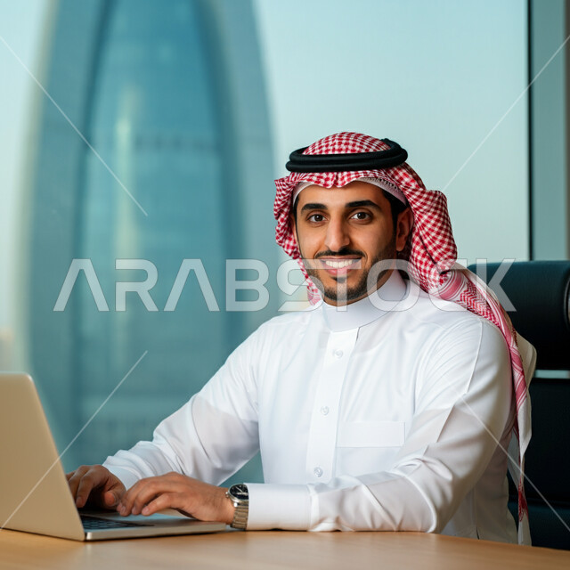 استخدام الأجهزة التقنية الحديثة، إدارة شؤون الأعمال وتنظيمها، صورة مقربة لرجل عربي خليجي سعودي يرتدي الشماغ و الثوب التقليدي يعمل على الحاسوب المحمول داخل مقر الشركة، مهن ووظائف إدارية مكتبية في المملكة العربية السعودية