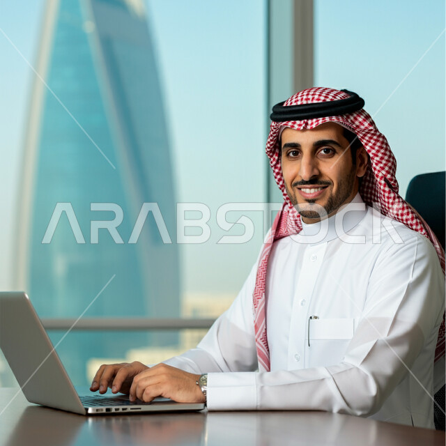 إدارة شؤون الأعمال وتنظيمها عبر الأجهزة التقنية، صورة مقربة لرجل عربي خليجي سعودي يرتدي الشماغ و الثوب التقليدي يعمل على الحاسوب المحمول داخل مقر الشركة، مهن ووظائف إدارية مكتبية في المملكة العربية السعودية، دمج العمل مع التقنية والتكنولوجيا