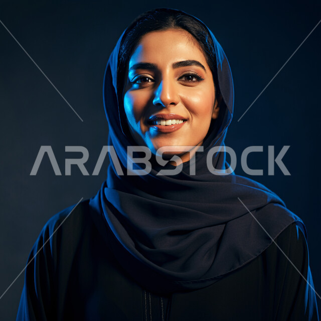 مفهوم النعومة والانوثة، أزياء محجبات عصرية راقية، الأناقة والاهتمام بالمظهر الخارجي، بورتريه مقرب لامرأة عربية خليجية سعودية مبتسمة ترتدي العباءة السوداء تنظر الى الكاميرا بإيماءات السرور والثقة بالنفس والفرح، خلفية سوداء