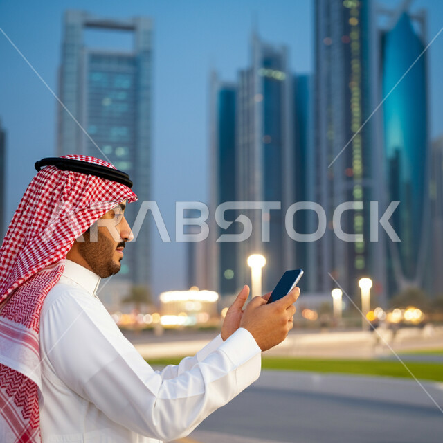 التواصل مع الأهل والأصدقاء، صورة مقربة من الجانب لرجل عربي خليجي سعودي يرتدي الثوب التقليدي والشماغ يمسك بيده الهاتف المحمول، استخدام الأجهزة التقنية الحديثة، التقاط الصور التذكارية وسط المدينة، إجراء مكالمات الفيديو عبر الموبايل، خلفية الأبراج وناطحات السحاب