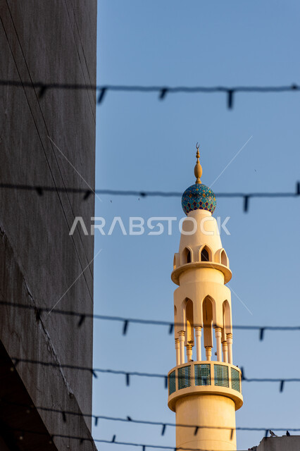 A mosque minaret in the middle of buildings in Bur Dubai area in Dubai, the architectural art of building mosques in the Arab Islamic style in the United Arab Emirates, a call for Muslims to perform religious duties and prayers, the concept of worship and drawing closer to God