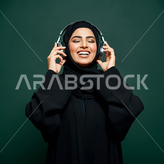 قضاء وقت ممتع, استخدام الهيدفون في اوقات الفراغ، بورتريه مقرب لإمرأه عربيه سعوديه خليجيه محجبة ترتدي عباءة سوداء مع سماعة الرأس بايماءات الإندماج والتفاعل وسماع الموسيقى، مفهوم التسليه والترفيه, تطور التقنيه والتكنولوجيا، خلفية خضراء