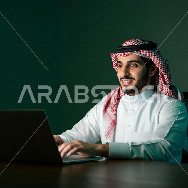 استخدام الأجهزة التقنية الحديثة، إدارة شؤون الأعمال وتنظيمها، بورتريه مقرب لرجل عربي خليجي سعودي يرتدي الشماغ و الثوب التقليدي يجلس على كرسي مريح يعمل على الحاسوب المحمول، مهن ووظائف إدارية، مفهوم إنجاز المشاريع والمهام، العمل عن بعد، خلفية خضراء