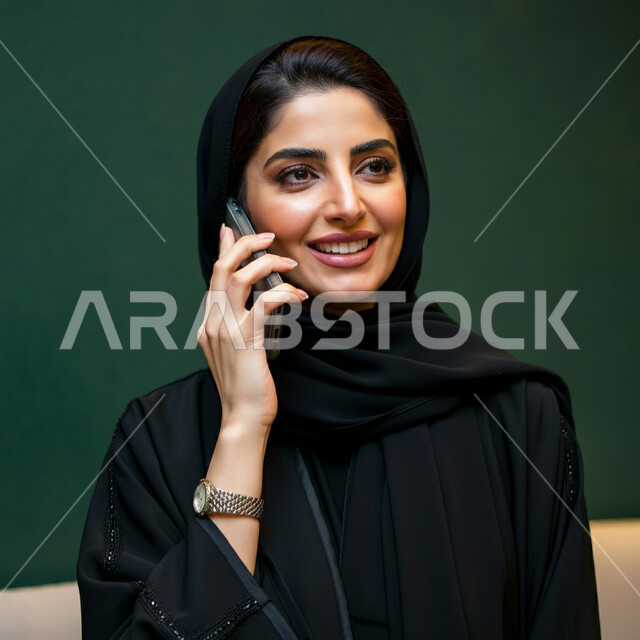الإجابة والرد على الاتصالات بإستخدام الهاتف المحمول، بورتريه مقرب لامرأة عربية سعودية خليجية محجبة تقوم بإجراء مكالمة صوتية عبر الجوال، تعابير الفرح عند سماع الاخبار السارة، قضاء اوقات ممتعة بتبادل الاخبار والأحاديث، التواصل والاطمئنان على الأصدقاء، خلفية خضراء