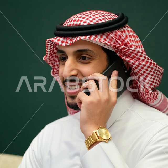 الإجابة والرد على الاتصالات بإستخدام الهاتف المحمول، بورتريه مقرب لرجل عربي سعودي خليجي يرتدي الثوب التقليدي يقوم بإجراء مكالمة صوتية، تعابير الفرح عند سماع الاخبار السارة، قضاء اوقات ممتعة بتبادل الاخبار والأحاديث، التواصل والاطمئنان على الأصدقاء، خلفية خضراء
