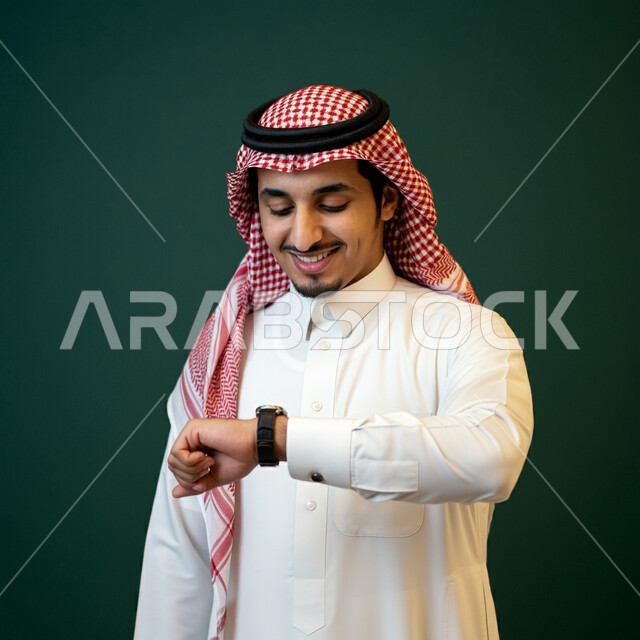 The concept of organizing and managing time, fixed reminders and alerts, the concept of manliness and interest in outward appearance, gestures of looking at the watch and setting appointments, a close-up portrait of a Saudi Arabian Gulf man wearing a traditional shemagh and thobe, wearing a watch on his hand and following it, green background
