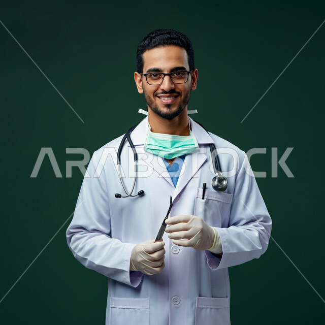  الفحص الطبي وتقديم الخدمات للمرضى بكل كفاءة، بورتريه لطبيب عربي خليجي سعودي مبتسم يرتدي اليونيفورم الخاص بالعمل مع السماعة الطبي يقف باستقامة، مفهوم الطب والرعاية الصحية، النظر الى الكاميرا بتعابير السرور والفرح، العمل في القطاع الصحي، خلفية خضراء