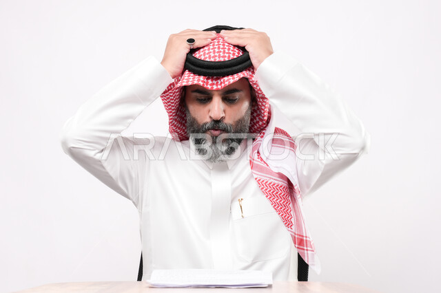 الإحساس بالصداع والمعاناة من آلام الرأس، بورتريه مقرب لرجل كبير بالسن عربي خليجي سعودي يرتدي الثوب التقليدي والشماغ يضع يده على رأسه بإيماءات التعب والإرهاق, مراجعة ومتابعة الخطط والمشاريع المكتبة, خلفية بيضاء