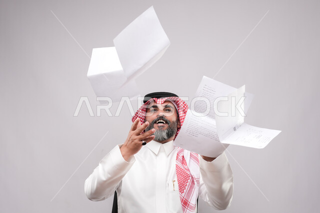 التقارير الخاصة بالعمل، بورتريه مقرب لرجل كبير بالسن عربي خليجي سعودي يرتدي الثوب التقليدي والشماغ ينظر الى الاعلى يقوم برمي مجموعة من الاوراق البيضاء, ايماءات السعادة والفرح لتحقيق الاهداف، خلفية بيضاء
