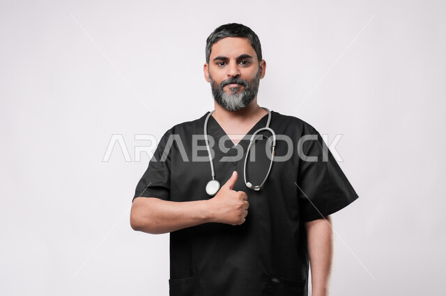 مفهوم الامتياز والجودة, الاستعداد لتقديم الخدمات للمرضى بكل كفاءه، مفهوم الطب والرعاية الصحية، بورتريه مقرب لطبيب كبير بالسن عربي خليجي يرتدي اليونيفورم وسماعة الفحص يقوم برفع اصبع الابهام للاعلى بتعابير القبول والموافقة، مهن ووظائف طبية في القطاع الصحي, خلفية بيضاء