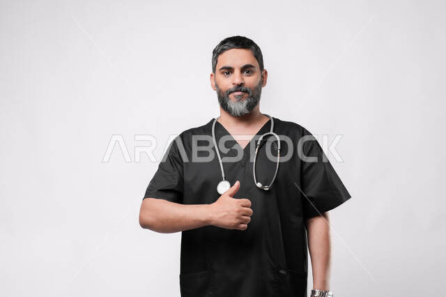 مفهوم الامتياز والجودة, الاستعداد لتقديم الخدمات للمرضى بكل كفاءه، مفهوم الطب والرعاية الصحية، بورتريه مقرب لطبيب كبير بالسن عربي خليجي يرتدي اليونيفورم وسماعة الفحص يقوم برفع اصبع الابهام للاعلى بتعابير القبول والموافقة، مهن ووظائف طبية في القطاع الصحي, خلفية بيضاء