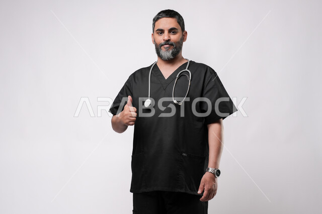 مفهوم الامتياز والجودة, الاستعداد لتقديم الخدمات للمرضى بكل كفاءه، مفهوم الطب والرعاية الصحية، بورتريه لطبيب كبير بالسن عربي خليجي يرتدي اليونيفورم الطبي وسماعة الفحص يقوم برفع اصبع الابهام للاعلى بتعابير القبول والموافقة، مهن ووظائف طبية في القطاع الصحي, خلفية بيضاء