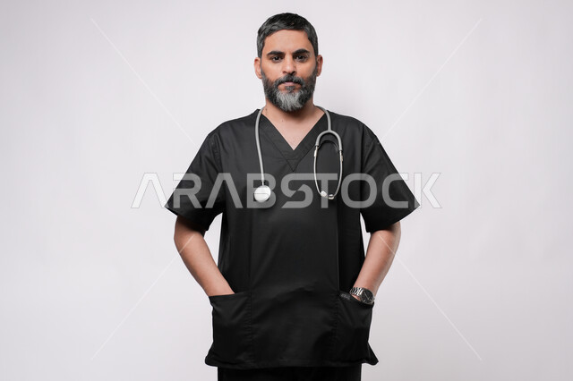 الاستعداد لتقديم الخدمات للمرضى بكل كفاءه، مفهوم الطب والرعاية الصحية، بورتريه لطبيب كبير بالسن عربي خليجي يرتدي اليونيفورم الطبي وسماعة الفحص ينظر الى الكاميرا بايماءات الفرح والسعادة، مهن ووظائف طبية في القطاع الصحي, خلفية بيضاء
