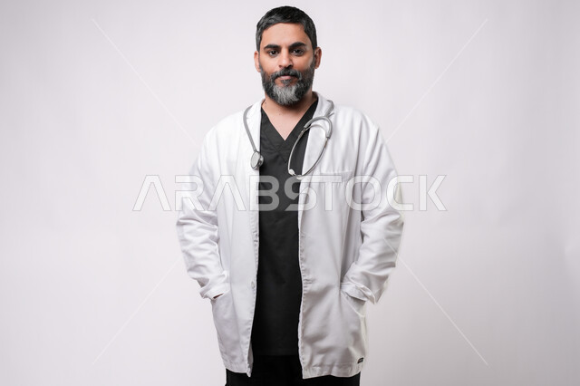 الاستعداد لتقديم الخدمات للمرضى بكل كفاءه، مفهوم الطب والرعاية الصحية، بورتريه لطبيب كبير بالسن عربي خليجي يرتدي المعطف الطبي والسماعه ينظر الى الكاميرا بايماءات الفرح والسعادة، مهن ووظائف طبية في القطاع الصحي, خلفية بيضاء