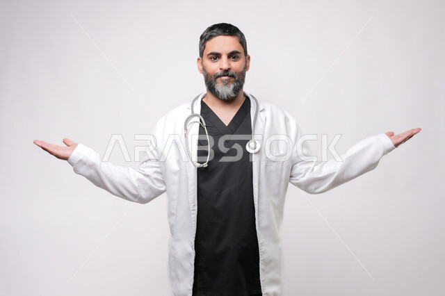 الترحيب والاستقبال ببشاشة، بورتريه لطبيب مسن عربي سعودي خليجي يرتدي يرتدي المعطف الطبي والسماعه ينظر الى الكاميرا يفتح كفيه بايماءات السرور برؤية شخص ما، الاستعداد لتقديم الخدمات للمرضى بكل كفاءه، مفهوم الطب والرعاية الصحية، الإشارة نحو هدف معين، خلفية بيضاء