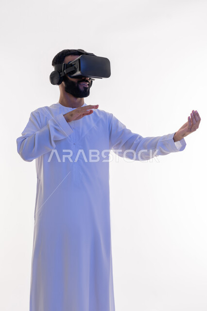 حمل ورفع شيء ما، التفاعل مع الفيلم ومحاكاة العالم الخيالي، بورتريه لرجل عربي خليجي اماراتي يرتدي الكندورة يقوم بمشاهدة أفلام عبر نظارات الواقع الافتراضي ثلاثية الأبعاد يفتح يده لامساك العناصر الهولوجرامية, ايماءات الاندماج والمتعة, خلفيه بيضاء