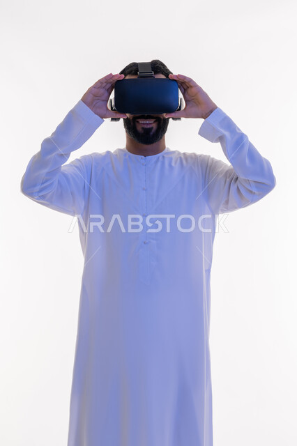 التفاعل مع الفيلم ومحاكاة العالم الخيالي، بورتريه لرجل عربي خليجي اماراتي مبتسم يرتدي الكندورة التقليدية يقوم بمشاهدة أفلام عبر نظارات الواقع الافتراضي ثلاثية الأبعاد, ايماءات تدل على الاندماج والمتعة, خلفيه بيضاء