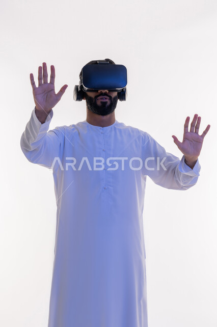 تعابير وايماءات الدفاع عن النفس, الاندماج ومحاولة امساك شيء ما, بورتريه لرجل عربي خليجي اماراتي يرتدي الكندورة و نظارات الواقع الافتراضي يقوم بالتفاعل ومحاكاة العالم الخيالي، تقنيات حديثة وأجهزة تكنولوجية، خلفية بيضاء