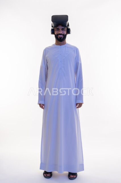 النظر الى الكاميرا بتعابير السعادة والسرور، التفاعل مع الفيلم ومحاكاة العالم الخيالي، بورتريه لرجل عربي خليجي اماراتي يرتدي الكندورة يقوم بمشاهدة أفلام عبر نظارات الواقع الافتراضي ثلاثية الأبعاد, ايماءات الاندماج والمتعة,  الجسم بالطول الكامل، خلفيه بيضاء