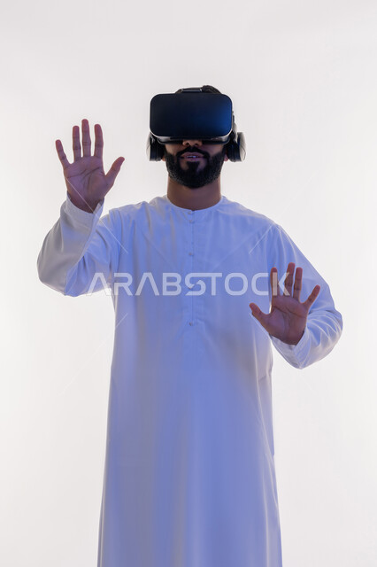 تعابير وايماءات الدفاع عن النفس, الاندماج ومحاولة امساك شيء ما, بورتريه لرجل عربي خليجي اماراتي يرتدي الكندورة و نظارات الواقع الافتراضي يقوم بالتفاعل ومحاكاة العالم الخيالي، تقنيات حديثة وأجهزة تكنولوجية، خلفية بيضاء