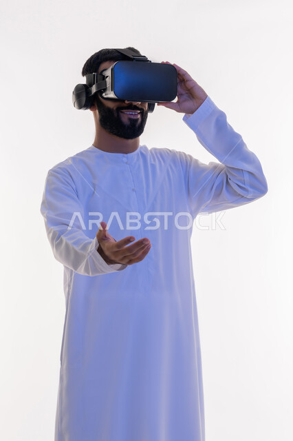 التفاعل مع الفيلم ومحاكاة العالم الخيالي، رفع وحمل شيء ما، بورتريه لرجل عربي خليجي اماراتي يرتدي الكندورة يقوم بمشاهدة أفلام عبر نظارات الواقع الافتراضي ثلاثية الأبعاد يمد كفه الى الامام, ايماءات الاندماج والمتعة, خلفيه بيضاء
