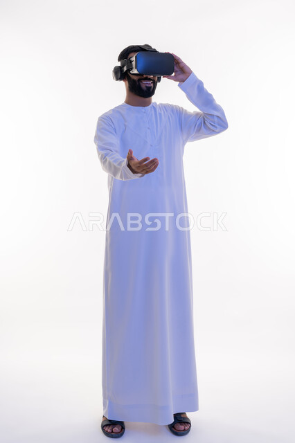 رفع وحمل شيء ما، التفاعل مع الفيلم ومحاكاة العالم الخيالي، بورتريه لرجل عربي خليجي اماراتي يرتدي الكندورة يقوم بمشاهدة أفلام عبر نظارات الواقع الافتراضي ثلاثية الأبعاد يمد كفه الى الامام, ايماءات الاندماج والمتعة,  الجسم بالطول الكامل، خلفيه بيضاء