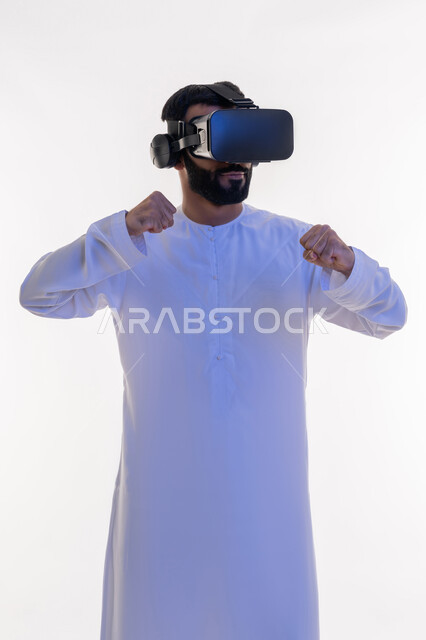 التدرب على الحركات القتالية من خلال ألعاب الفيديو، تفريغ الطاقة السلبية، ممارسة رياضة الدفاع عن النفس بتقنيات تكنولوجية، بورتريه لرجل عربي خليجي اماراتي مبتسم يرتدي الكندورة ونظارات الواقع الافتراضي بإيماءات الملاكمة والمصارعة، خلفية بيضاء