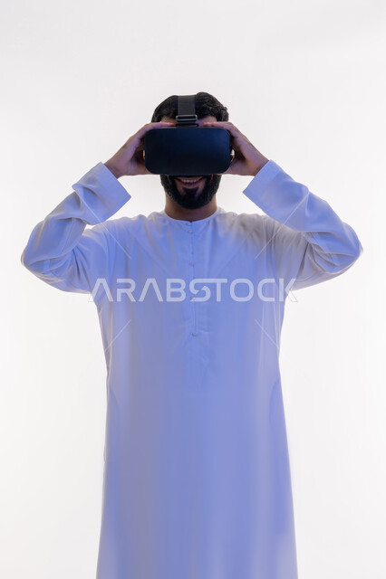التفاعل مع الفيلم ومحاكاة العالم الخيالي، بورتريه مقرب لرجل عربي خليجي اماراتي مبتسم يرتدي الكندورة التقليدية يقوم بمشاهدة أفلام عبر نظارات الواقع الافتراضي ثلاثية الأبعاد, ايماءات تدل على الاندماج والمتعة, خلفيه بيضاء
