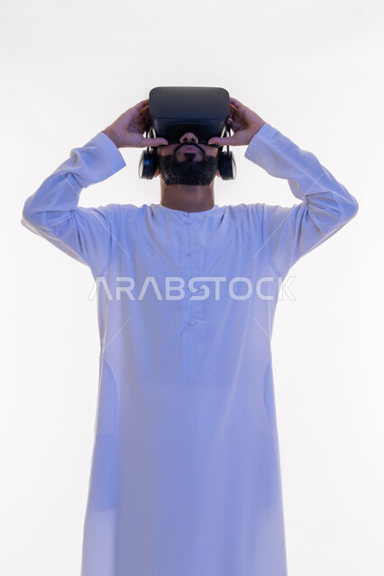 Interacting with the movie and simulating the imaginary world, close-up portrait of a smiling Emirati Gulf Arab man wearing a traditional kandura watching movies through 3D virtual reality glasses, gestures indicating integration and enjoyment, white background