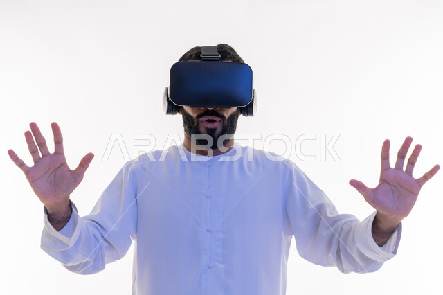 الاندماج ومحاولة امساك شيء ما، التفاعل ومحاكاة العالم الخيالي, بورتريه مقرب لرجل عربي خليجي اماراتي يرتدي الكندورة و نظارات الواقع الافتراضي بايماءات الدفاع عن النفس, تقنيات حديثة وأجهزة تكنولوجية، خلفية بيضاء